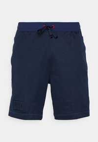 Pantalones cortos deportivos azul marino hechos de una tela suave, con una cinturilla elástica y cordones rojos, y un parche de logo texturizado en la pierna izquierda.