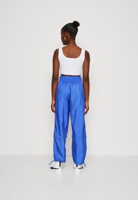Pantalones ligeros azules con cintura elástica, piernas ajustadas y cordón en los tobillos. Combinados con un top corto blanco ajustado.