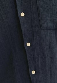 Donkerblauwe shirts met textuur, voorzien van een knoopsluiting aan de voorkant met grote, roomkleurige knopen en een borstzakdetail.