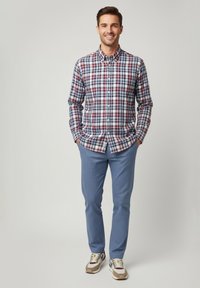 Camisa de hombre con botones en patrón a cuadros que combina colores azul, blanco y rojo, acompañada de pantalones texturizados azul claro y zapatillas informales multicolores.