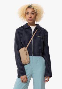 Veste cropped rayée bleu marine avec fermeture éclair sur le devant, associée à un pantalon texturé bleu clair et un sac en bandoulière beige.