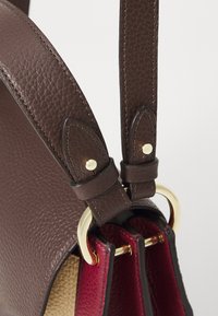 Sac à main en cuir marron avec une surface texturée, accents en métal doré et un intérieur doux comportant des sections rouges et beiges. Bandoulières ajustables.