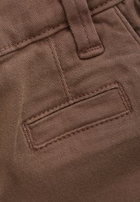 Brunt tygficka med sömmar, med en platt design och slät textur, som är en del av ett par byxor eller shorts.