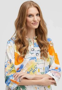 Bunte, bedruckte Hemdbluse mit verschiedenen Designs, darunter Sonnenmotive und Fahrzeuge auf einem weißen Grund. Weicher, leichter Stoff.