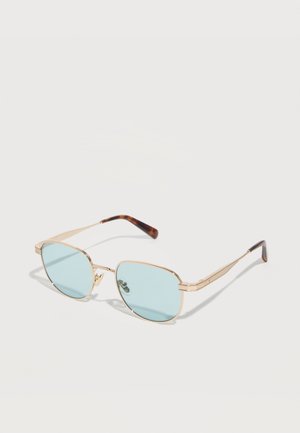 Slnečné okuliare so zlatým rámom, svetlomodrými obdĺžnikovými sklami a koncovkami s motívom korytnačej mušle, položené na bielom povrchu.