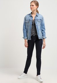 Lichtblauwe spijkerjack met knoopsluiting, gecombineerd met een donkergrijze top en donkere skinny jeans. Witte sneakers maken de outfit compleet.