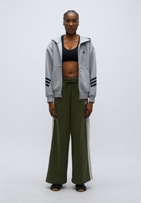 Γκρι φούτερ με φερμουάρ και μαύρες ρίγες, φορεμένο πάνω από μαύρο αθλητικό σουτιέν και χακί παντελόνι φαρδύ με λευκές πλαϊνές ρίγες, συνδυασμένο με μαύρα παπούτσια.