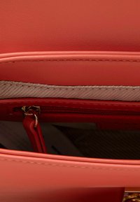 Borsa sintetica corallo con interno dotato di scomparto con cerniera, caratterizzato da un rivestimento beige morbido e accessori in oro.