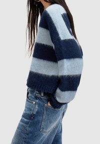 Sweter w paski z dzianiny w ciemnych i jasnoniebieskich odcieniach, o luźnym kroju, z zaokrąglonym dekoltem i ściągaczami na rękawach. W połączeniu z wysokim stanem jeansów.