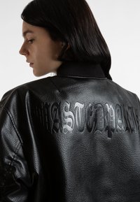 Čierna kožená bomber bunda s embosovaným textom "Wasted Paris" na chrbte, rebrovaným golierom a štruktúrovaným povrchom.