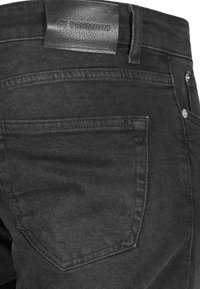 Gros plan sur la poche arrière d'un jean en denim noir avec une étiquette en cuir noir portant l'inscription 2Y PREMIUM au-dessus de la poche.