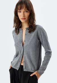 Cárdigan de punto gris con cuello redondo, mangas largas y seis botones en la parte delantera. Textura suave, corte recto y diseño minimalista.
