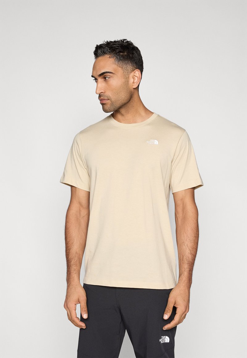 Μπεζ κοντομάνικο μπλουζάκι με στρογγυλή λαιμόκοψη και λευκό λογότυπο στο αριστερό στήθος. Το ύφασμα φαίνεται μαλακό με λεία υφή.