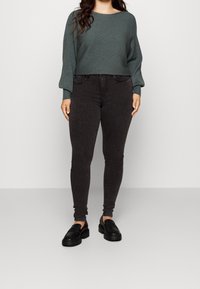 Pull vert en maille côtelée, coupe courte avec larges manches, assorti à un jean skinny noir taille haute et des mocassins noirs.