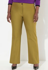 Uppvikta byxor i olivgrön tyg med en slät textur, med knappstängning fram och sidofickor. Bärs tillsammans med svarta klackar.