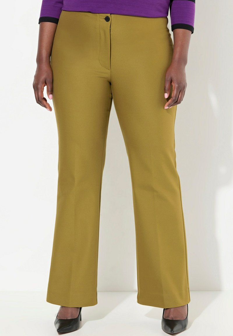 Uppvikta byxor i olivgrön tyg med en slät textur, med knappstängning fram och sidofickor. Bärs tillsammans med svarta klackar.