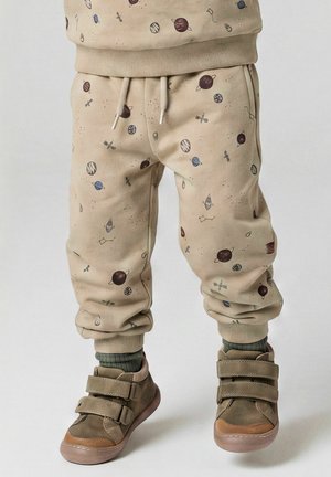 Pantalon beige pour enfants avec des imprimés sur le thème de l’espace, associé à des chaussettes vertes et des baskets beiges à scratch.