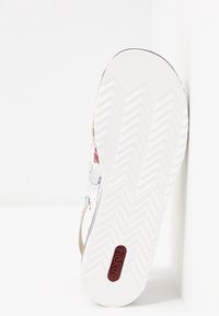 Vita sneaker med en texturerad gummisula, prydd med färgglada blommönster på en silverbakgrund och en bordeaux logo på hälen.