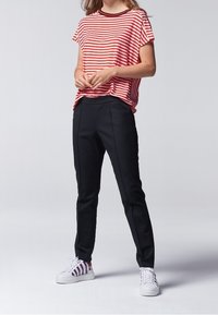 T-shirt à manches courtes rayé rouge et blanc, associé à un pantalon noir sur mesure et des chaussures blanches à rayures multicolores.