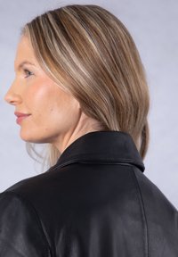 Black leather jacket featuring a large collar, smooth texture, and a tailored fit, shown from the side with hair cascading over the shoulder.