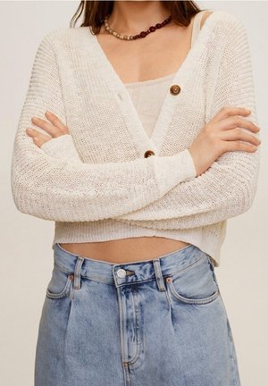 Cardigan en tricot crème clair avec un col en V et deux boutons. Porté par-dessus un haut beige, assorti à un jean en denim bleu clair taille haute.