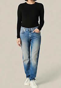 Top nero a maniche lunghe abbinato a jeans azzurri con effetto sbiadito. Il modello indossa scarpe da ginnastica bianche. Design semplice e classico.