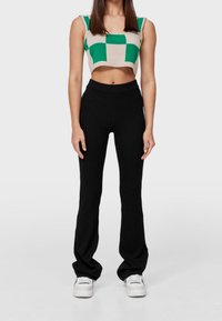 Geribbelde zwarte flared broek met hoge taille, gecombineerd met een cropped top in een beige en groen ruitpatroon. Soepele textuur en getailleerd ontwerp.