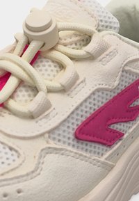 Krupan plan bež tenisice s mrežastim tkanjem, krem vezicama s kopčom i jarko ružičastim stiliziranim znakom sa strane.