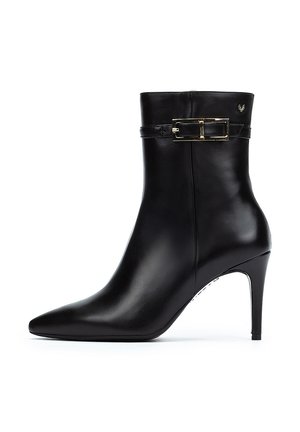 Bottine en cuir noir avec un bout pointu, un talon aiguille mince et un détail de sangle avec boucle décorative à la cheville. Texture lisse.