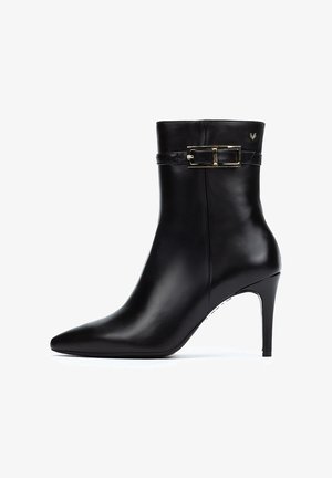 Botín de cuero negro hasta el tobillo con punta afilada, tacón de aguja delgado y un detalle de hebilla decorativa en el tobillo. Textura suave.