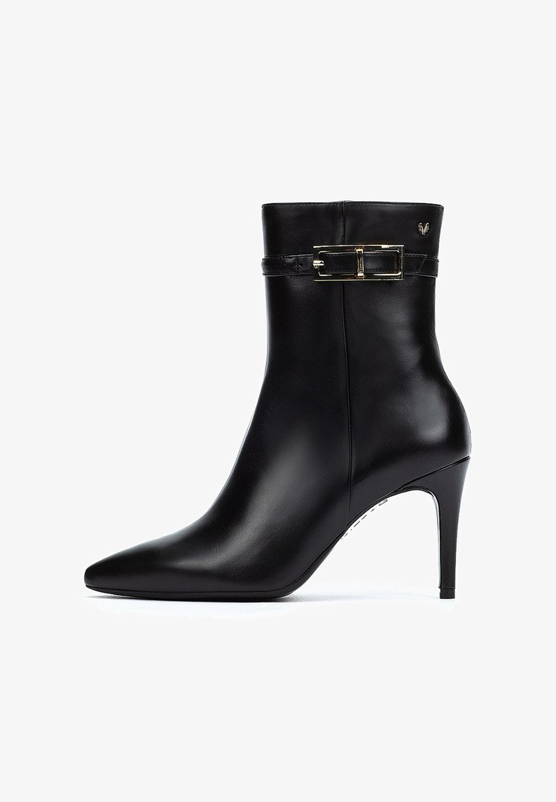 Botín de cuero negro hasta el tobillo con punta afilada, tacón de aguja delgado y un detalle de hebilla decorativa en el tobillo. Textura suave.