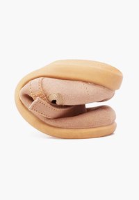 Zapato plegable suave y beige hecho de tela, con una forma redondeada y una suela de goma suave y flexible. Presenta detalles de costura y un diseño de plegado único.