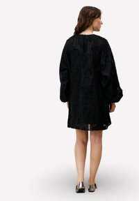 Robe noire transparente à motif floral, manches longues bouffantes et col rond simple. Texture douce et coupe décontractée.