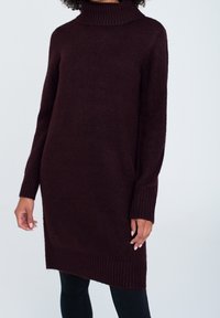 Kastanjebrun polotröja i en mjuk, texturerad stickning, med långa ärmar och ribbat avslut, kombinerad med svarta, figursydda byxor.