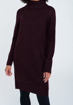 Bordeauxfarbener Rollkragenpullover aus einem weichen, strukturierten Strick, mit langen Ärmeln und geripptem Saum, kombiniert mit schwarzen, figurbetonten Hosen.