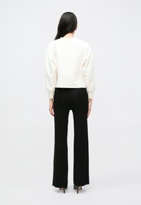 Λευκό cropped φούτερ με στρογ γυλή λαιμόκοψη και φουσκωτά μανίκια, σε συνδυασμό με μαύρο παντελόνι καμπάνα. Λεία ύφανση με ριμπ υφή.