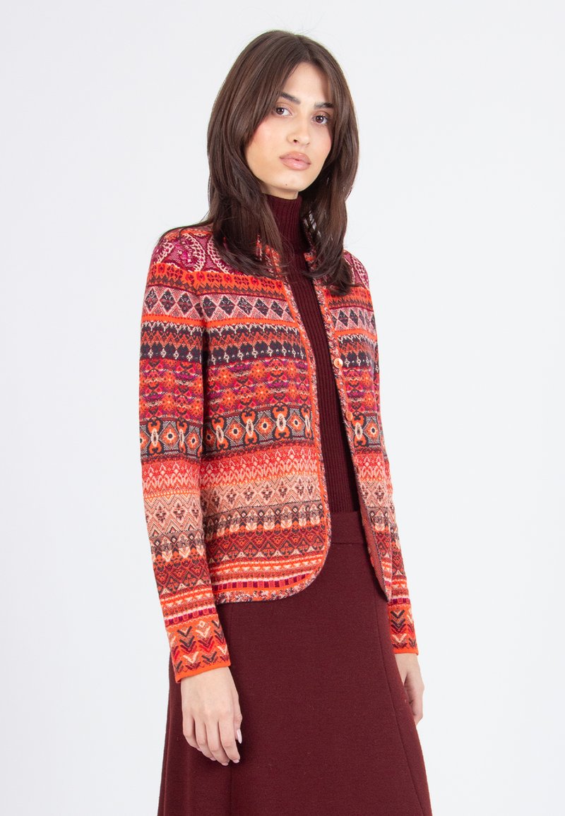 Strickjacke mit einem aufwendigen mehrfarbigen geometrischen Muster, hauptsächlich in Rot, Orange und Rosa. Rundhalsausschnitt, cropped Länge.