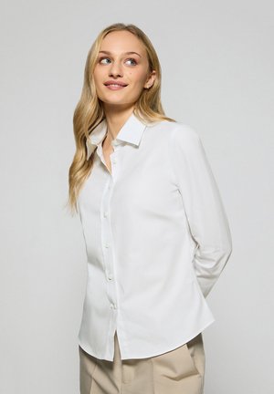 Witte blouse met een puntkraag, lange mouwen en een rechte pasvorm. De stof lijkt glad en lichtgewicht. Eenvoudig ontwerp, zonder patronen.