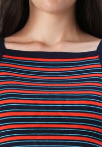 Haut côtelé rayé rouge, marine et bleu clair avec un col carré et une coupe ajustée, mettant en valeur une texture lisse et une répartition uniforme des couleurs.