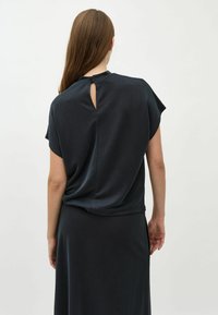 Schwarzes Kurzarmoberteil mit lockerem Schnitt, das ein Schlüssellochdetail am Rücken und eine weiche Textur aufweist. Der Stoff wirkt glatt und leicht.