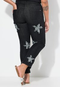 Vaqueros de denim negros con parches en forma de estrella, detalles desgastados y un diseño ajustado. Presentan bolsillos y una cinturilla de altura media.