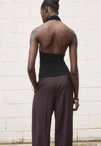 Black halter top with a fitted bodice paired with loose, brown trousers. The outfit features smooth fabric and minimalistic gold hardware accents.