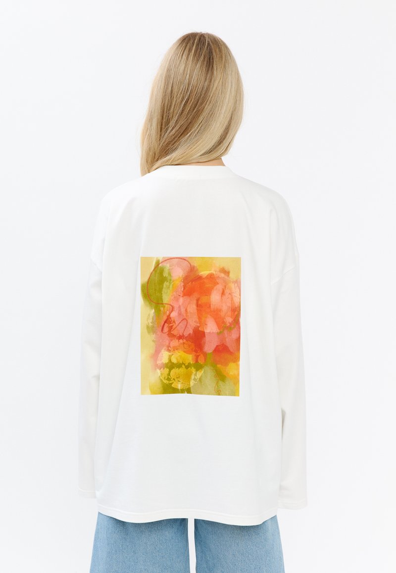 Witte lange mouwen T-shirt met een levendige bloemenprint in roze, geel en groen op de achterkant. Losse pasvorm met verlaagde schouders.