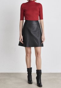 Röd ribbad kortärmad topp kombinerad med en svart läder A-linjeformad kjol. Outfitten har en figurnära design, slät textur och svarta stövlar som når upp till anklarna.