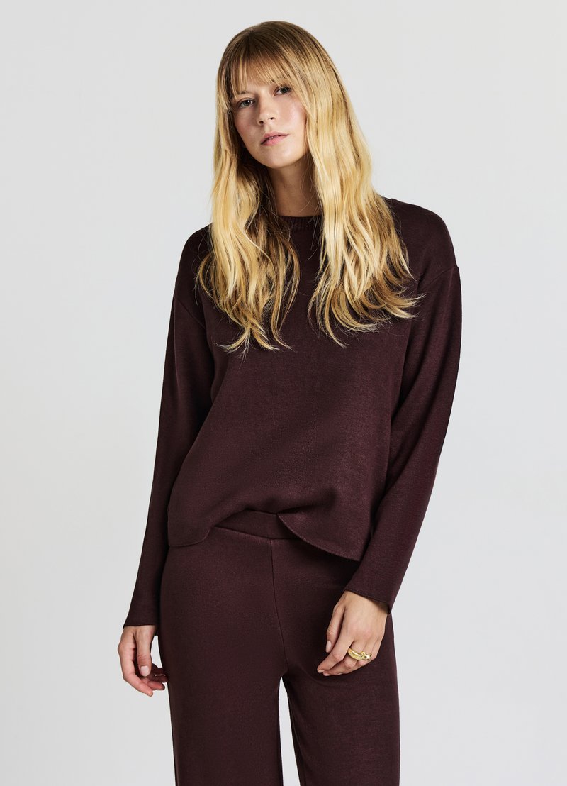 Bordeauxroter Pullover mit langen Ärmeln, strukturierter Stoff und lockerer Passform, kombiniert mit passenden, hoch taillierten Hosen. Minimalistisches Design.