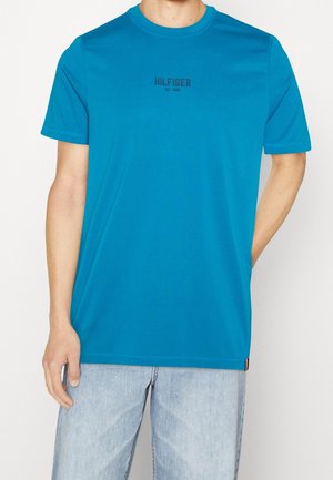 Turkis T-shirt lavet af blødt stof med rund halsudskæring og korte ærmer. "HILFIGER" logo i sort tværs over brystet.