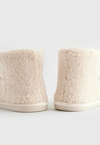 Bottines beige doublées en polaire, avec une surface texturée, une sensation douce et une semelle beige robuste, présentant une hauteur courte et un design simple.