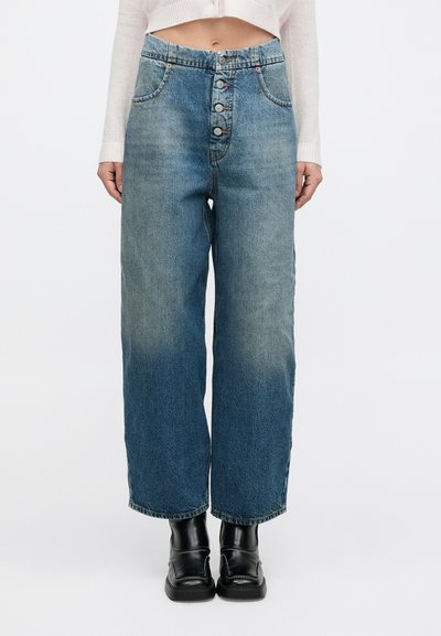 Light blue denim jeans with a high waist, wide legs, five-button closure, and slight fading throughout. Styled with black ankle boots.