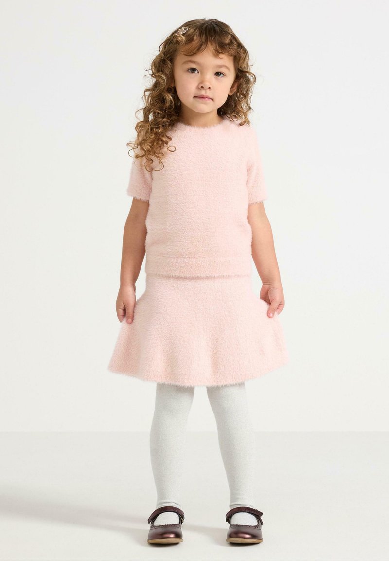 Rosa, flauschiges kurzärmliges Oberteil, kombiniert mit einem ausgestellten Rock und hellgrauen Strumpfhosen. Dazu braune Schuhe mit einem Riemen und insgesamt einer weichen Textur.