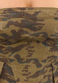 Gros plan d’un tissu camouflage vert et marron avec des coutures visibles et un tissage texturé.